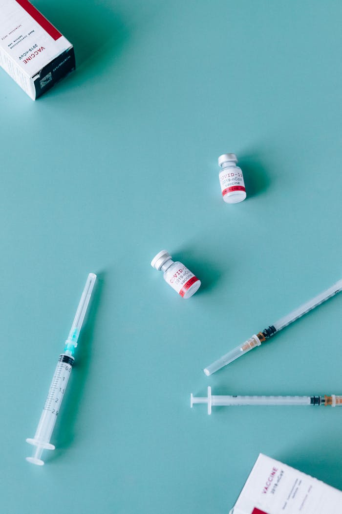 Top-down view of vaccine vials and syringes for COVID-19 vaccination on a teal background.