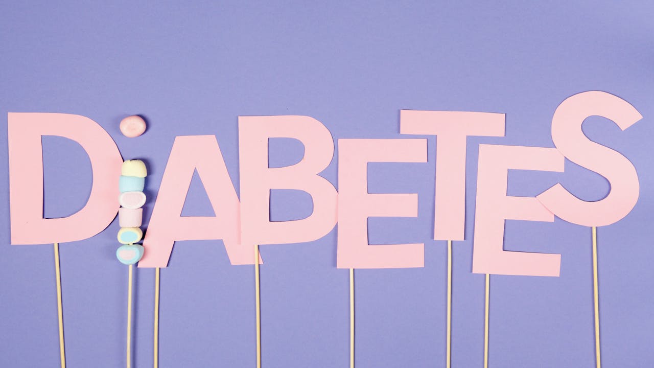 Pink paper letters spelling 'Diabetes' on sticks against a blue background, symbolizing awareness.